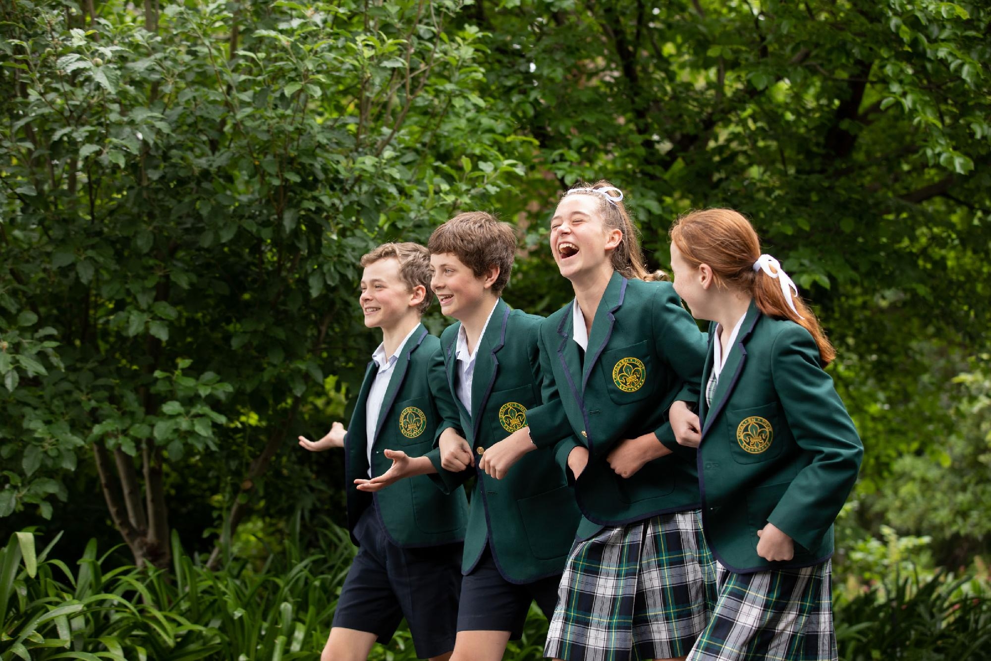 Four Mercedes College students laughing and linking arms while walking outdoors.